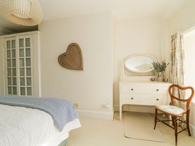 A bedroom with a bed blue blanket white dresser with mirror wooden chair and floral curtains at Clamoak Cottage Clamoak near Bere Alston