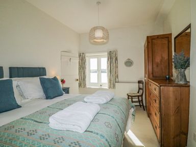 A bedroom with a bed with blue pillows white towels a wooden dresser and a window at Clamoak Cottage Clamoak near Bere Alston