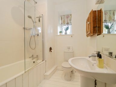 A bathroom with a bathtub and shower head a toilet and a sink with soap dispensers and a wooden cabinet on the wall at Clamoak Cottage in Clamoak near Bere Alston