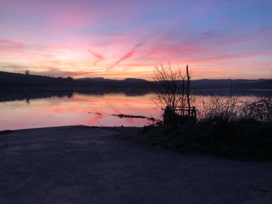 A lake at sunset with hills in the background and bare trees in the foreground at Clamoak Cottage Clamoak near Bere Alston