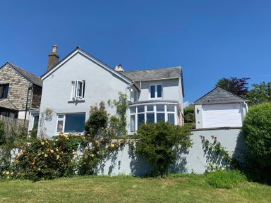A white cottage with multiple windows a garage and plants growing along the wall at Clamoak Cottage in Clamoak near Bere Alston