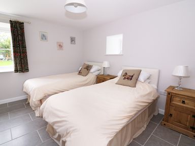 A bedroom with two single beds beige bedding wooden nightstands and a window with patterned curtains at Cilgwyn Bach in Llandysul