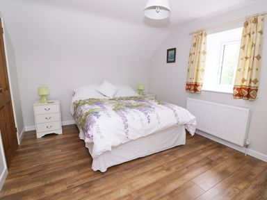 A bedroom with a double bed bedside tables with lamps a window with curtains and wooden flooring at Cilgwyn Bach in Llandysul