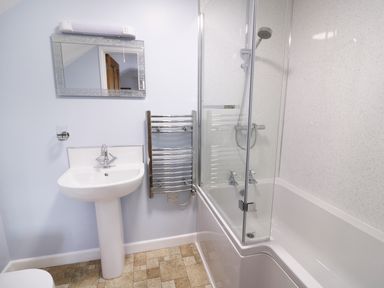 A bathroom with a sink and mirror next to a bathtub with shower and a towel radiator at Cilgwyn Bach in Llandysul