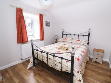 A bedroom with a metal bed with floral bedding a stuffed teddy bear two bedside tables lamps a window with curtains and wooden floor at Cilgwyn Bach in Llandysul