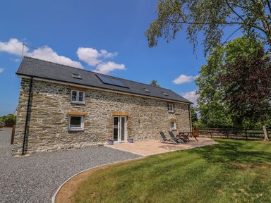 An outdoor view of a stone house with a tiled patio and garden area at Cilgwyn Bach in Llandysul