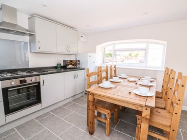 A kitchen with wooden dining table set with white dishes and modern cabinets at Cilgwyn Bach in Llandysul