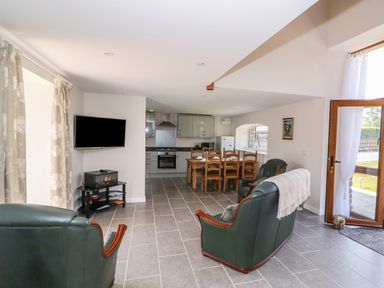 An open plan living room with green leather armchairs a dining table and chairs and a kitchen with grey cabinets at Cilgwyn Bach in Llandysul