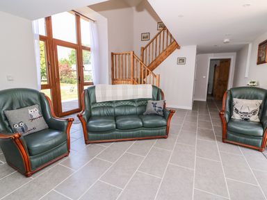 A living room with green leather sofa and chairs next to wooden staircase at Cilgwyn Bach in Llandysul