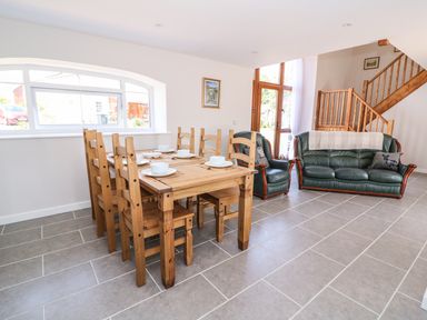 A dining area with a wooden table and chairs next to green leather sofas and wooden stairs at Cilgwyn Bach in Llandysul