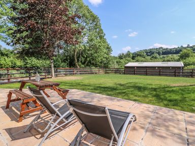 A patio with two lounge chairs and a wooden picnic table next to a grassy lawn and fenced yard at Cilgwyn Bach in Llandysul