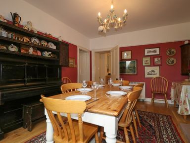 A dining room with wooden table set with plates and glasses wooden chairs and a decorated cabinet against a red wall at Dale House in Lorton