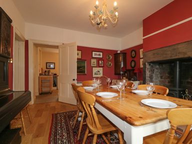 A dining room with wooden table and chairs set with plates and glasses a fireplace paintings on red walls and a chandelier at Dale House in Lorton
