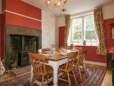 A dining room with a wooden table set for six next to a fireplace and a window with floral curtains at Dale House in Lorton