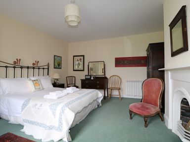 A bedroom with a bed with white linens and folded towels a wooden dresser with a mirror wooden chairs a pink upholstered chair a white fireplace and framed artwork at Dale House in Lorton