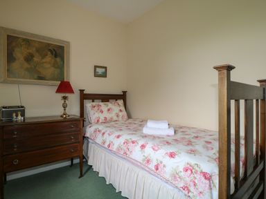 A small bedroom with a single wooden bed with floral bedding a wooden dresser with a red lamp and paintings on the wall at Dale House in Lorton