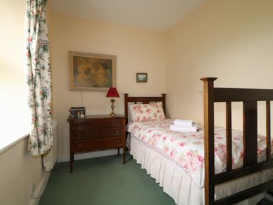 A bedroom with a single bed with floral bedding a wooden dresser with a lamp and pictures on the wall at Dale House in Lorton