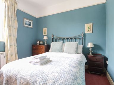 A bedroom with a metal headboard bed two side tables with lamps and framed pictures on blue walls at Dale House in Lorton