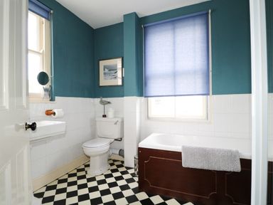 A bathroom with a bathtub a white toilet and a sink with a window covered by a blue blind at Dale House in Lorton