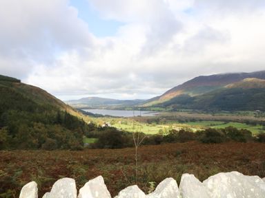 A valley with a lake surrounded by hills and fields with a stone wall in the foreground at Dale House in Lorton
