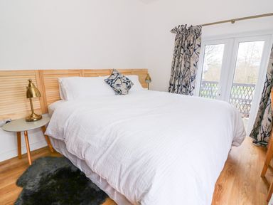 A bedroom with a large bed white bedding bedside table with lamp and patterned curtains at Crooked Hill Cottage in Ammanford