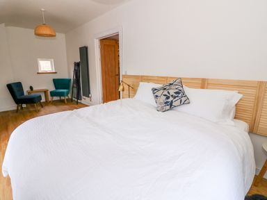 A bedroom with a large bed with white bedding a wooden headboard two upholstered chairs a small wooden table and a door at Crooked Hill Cottage in Ammanford