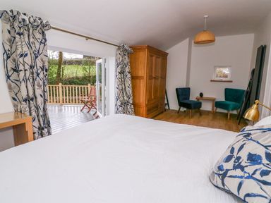 A bedroom with a bed and pillows a wooden wardrobe two chairs and a small table open doors to a deck outside at Crooked Hill Cottage in Ammanford