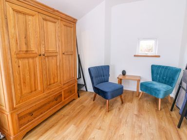 A room with wooden wardrobe two blue chairs a small wooden table and a small window at Crooked Hill Cottage in Ammanford