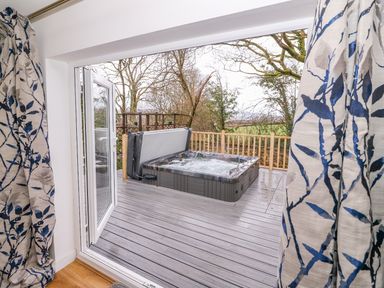 A view of an outdoor deck with a hot tub and trees beyond at Crooked Hill Cottage in Ammanford