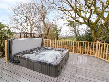 An outdoor hot tub on a wooden deck surrounded by trees at Crooked Hill Cottage in Ammanford