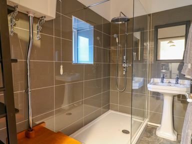 A bathroom with a shower area a pedestal sink and a window at Crooked Hill Cottage in Ammanford