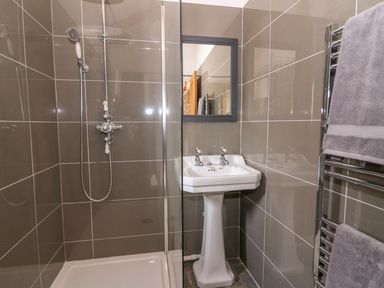 A bathroom with a shower area white pedestal sink and a mirror above it at Crooked Hill Cottage in Ammanford