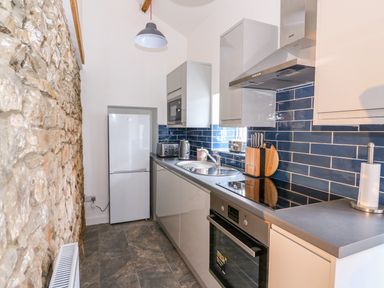 A kitchen with stone wall on one side white fridge and cabinets and blue tiled backsplash at Crooked Hill Cottage in Ammanford