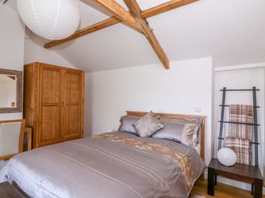 A bedroom with a double bed wooden wardrobe hanging racks with blankets and a wooden chair at Crooked Hill Cottage in Ammanford
