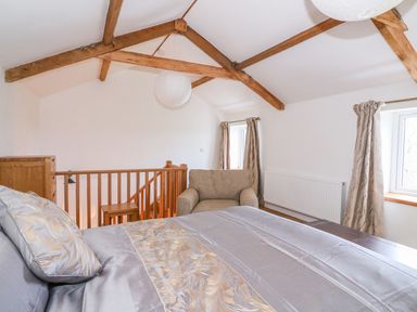 A bedroom with a bed armchair wooden railing and windows with curtains at Crooked Hill Cottage in Ammanford
