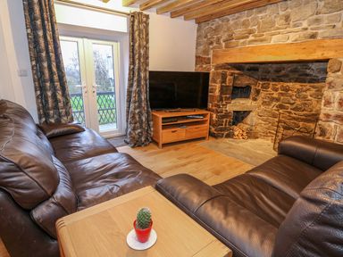 A living room with leather sofas a wooden table with a small plant a stone fireplace and a TV on a stand at Crooked Hill Cottage in Ammanford