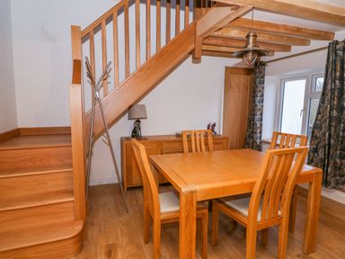 A dining area with wooden table and chairs under a wooden staircase at Crooked Hill Cottage in Ammanford