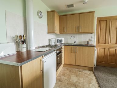 A kitchen with wooden cabinets a sink a stove a refrigerator and kitchen utensils at 2 Park Nook Close in Waberthwaite