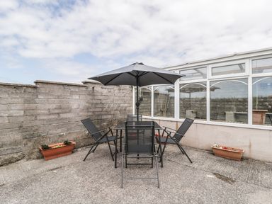 An outdoor patio area with a table umbrella and four chairs next to a brick wall and a conservatory at 2 Park Nook Close in Waberthwaite