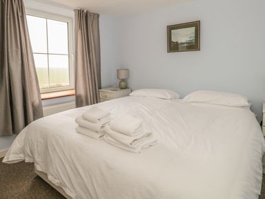 A bedroom with a large bed two pillows folded towels on the bed bedside tables with lamps a window and a framed picture on the wall at 2 Park Nook Close in Waberthwaite