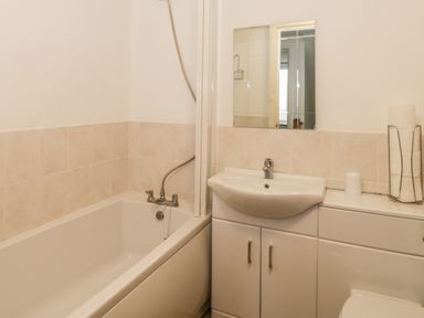 A bathroom with a bathtub a sink with cabinet a mirror and a toilet paper holder at 2 Park Nook Close in Waberthwaite