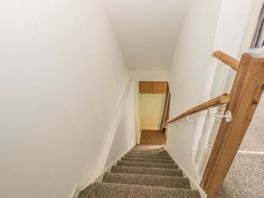 A carpeted staircase with wooden handrails leading downstairs at 2 Park Nook Close in Waberthwaite