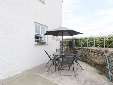 An outdoor patio with a glass table and black chairs under a black umbrella at 1 Park Nook Close in Waberthwaite