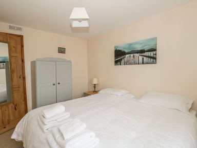 A bedroom with a double bed with white linens towels on it a wardrobe a nightstand with a lamp and wall art at 1 Park Nook Close in Waberthwaite