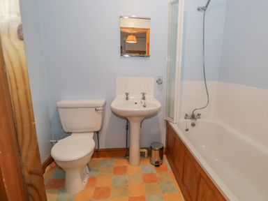 A bathroom with a toilet sink a bathtub with shower and a small trash bin at 1 Park Nook Close in Waberthwaite