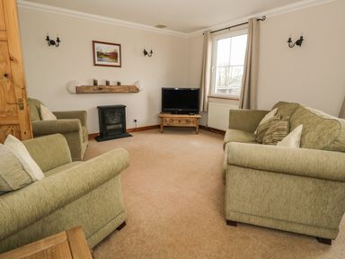 A living room with three green upholstered chairs a television on a wooden stand a window and wall-mounted lights at 1 Park Nook Close in Waberthwaite