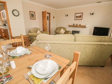 A dining table with place settings near a living room with sofas armchairs a television and wall art at 1 Park Nook Close in Waberthwaite