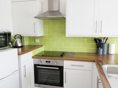 A kitchen with white cabinets green tiled backsplash stainless steel oven toaster kettle and utensils at Driftwood in Bude