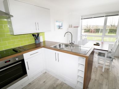 A kitchen with white cabinets wood countertop green backsplash and a dining table with chairs near a window at Driftwood in Bude