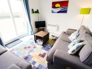 A living room with two gray sofas a colorful checkered rug a wooden crate coffee table a small TV and speakers on a green shelf at Driftwood in Bude